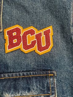 the bcu logo is embroidered on an old pair of blue jean's with yellow and red stitching