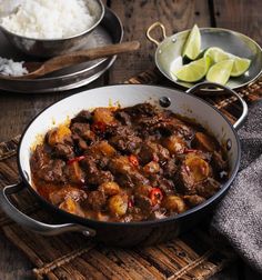 some food that is in a pan on a wooden table next to rice and limes