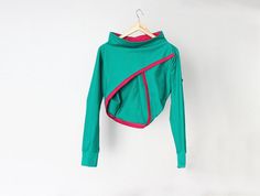 a green top hanging on a white wall with a red stripe down the side and pink trim around the neck