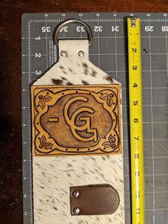 a wooden keychain with the letter g on it next to a ruler