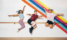 three young women jumping in the air with their arms spread out and one woman is holding her leg up