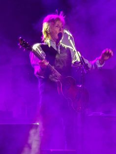 a man standing on top of a stage holding a guitar in his hand and singing into a microphone