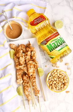 chicken skewers with peanut sauce and peanuts on a white plate next to a bottle of mustard