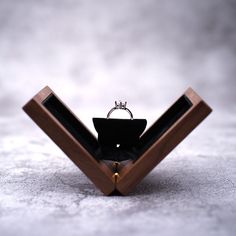 a wooden ring holder with a black bow tie on it's side and a diamond ring in the middle