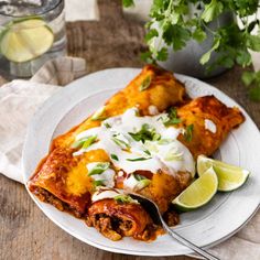 a white plate topped with two enchiladas next to a glass of water