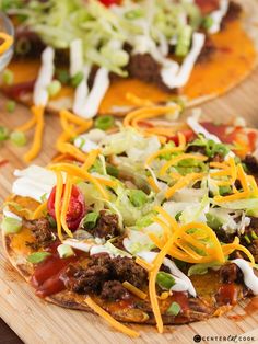 two tacos with meat, cheese and lettuce on them sitting on a cutting board