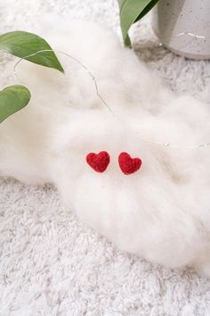 two red hearts are placed on top of white fluffy material next to a potted plant