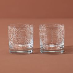 two clear glasses sitting next to each other on top of a brown surface with one glass in the middle