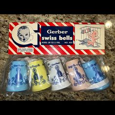 four different colored cups in plastic wrappers on a counter with an ad for gerber swiss bell