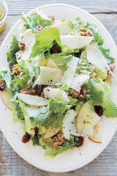 a white plate topped with lettuce and apple salad next to a glass of orange juice