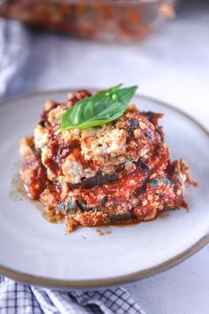 a white plate topped with lasagna covered in sauce and basil garnish