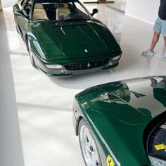 two green sports cars in a showroom with people looking at them on the floor