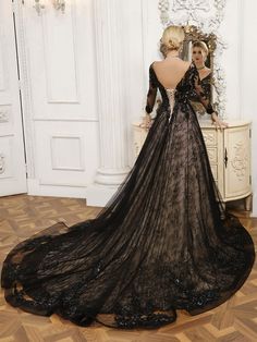 a woman in a black dress is looking at herself in the mirror while wearing an elaborately designed gown