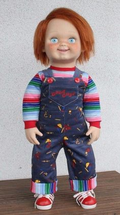 a doll with red hair and blue overalls on top of a wooden table in front of a white wall