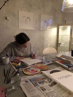 a woman sitting at a table with papers and paintbrushes in front of her