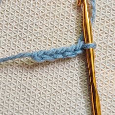 the crochet hook is laying on top of the knitted fabric with a golden knitting needle