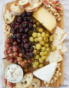 an assortment of cheeses, grapes and bread on a wooden platter with nuts