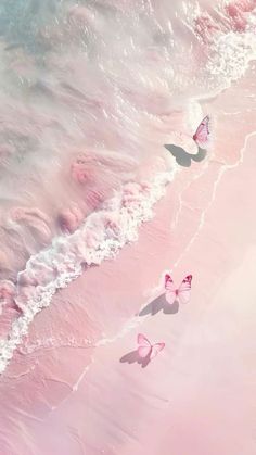 three pink butterflies are flying over the water at the edge of the beach, with waves coming in to shore