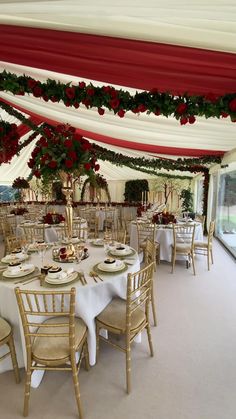 tables and chairs are set up for a formal function with red flowers on the ceiling