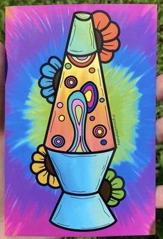 a hand holding up a colorful card with an image of a vase on it's side