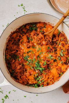 a pot filled with meat and cheese on top of a white counter next to a wooden spoon