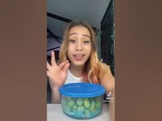 a young woman is making the peace sign with her hand while sitting in front of a plastic container filled with grapes