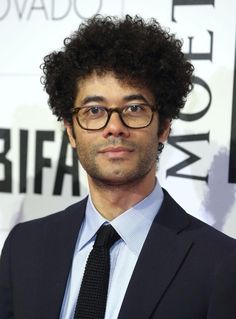 a man with curly hair wearing glasses and a suit