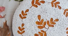 a cake with leaves painted on it sitting next to some flowers and leafy branches