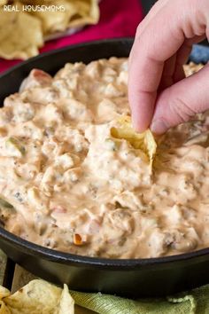 a hand dipping chips into a black bowl filled with white quesadilla dip