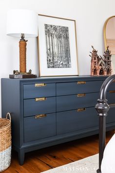 a blue dresser with gold handles and drawers in a white room next to a lamp