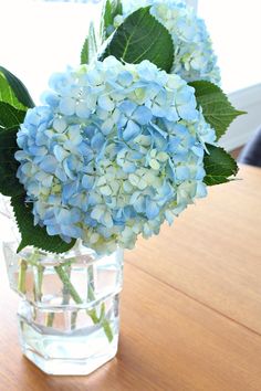 a glass vase filled with blue flowers on top of a wooden table