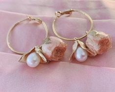 two pairs of gold hoop earrings with pearls and leaves on pink fabric background, closeup