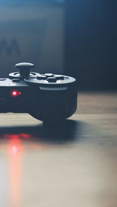 a video game controller sitting on top of a wooden table next to a window with red light coming from it