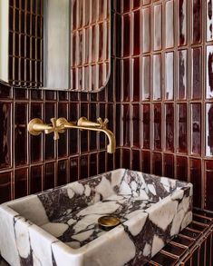 a marble sink in front of a mirror with gold faucet and tile on the wall