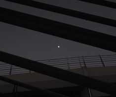 the moon is seen through some metal bars on a bridge overpass at night time