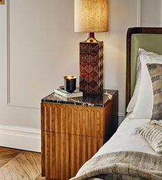 a nightstand with a candle and some books on it next to a bed in a room