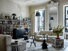 a living room filled with white furniture and lots of shelves full of bottles on the wall