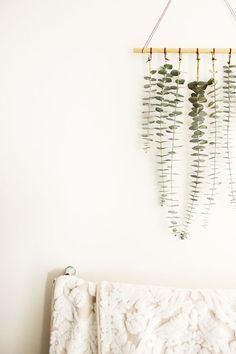 a plant hanging on the wall next to a bed with a white comforter underneath it