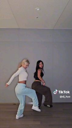 two women in white shirts and blue jeans are doing dance moves with one another on the floor