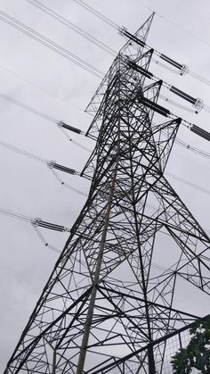 an electric tower with lots of wires above it and trees in the foreground on a cloudy day