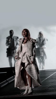 a woman is walking down the runway in a white dress and trench coat with her hands on her hips