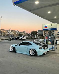 a light blue car is parked at a gas station with its hood up and the lights on