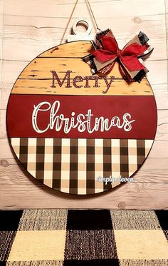 a merry christmas sign hanging on the side of a wooden wall next to a checkered rug