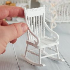 a miniature rocking chair is being held by someone's hand on a white wooden table