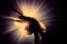 a woman is dancing in the dark with bright light shining through her hair and dress