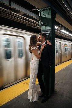 a man and woman are kissing in front of a train at a subway station as the train passes by