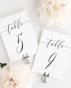 two place cards with the names of each table on them next to a white flower