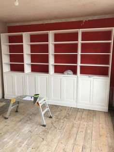 an empty room with red and white bookcases on the wall, two ladders in front of it