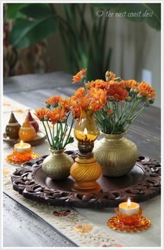 orange flowers in vases on a tray with candles