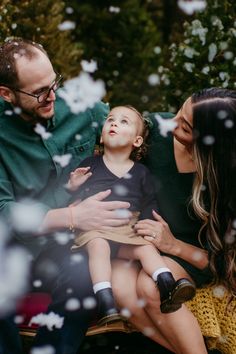 a man, woman and child are sitting on a bench with snow falling around them